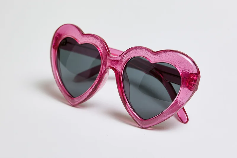 Heart-shaped sunglasses with translucent pink plastic frames on white background