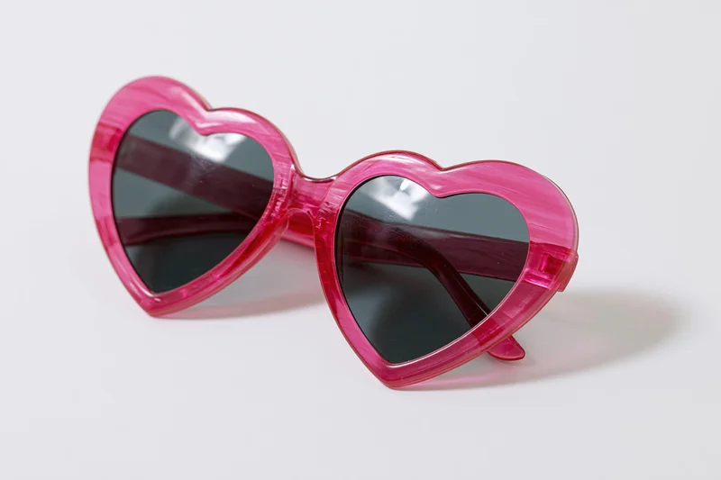 Heart-shaped pink plastic sunglasses on white background