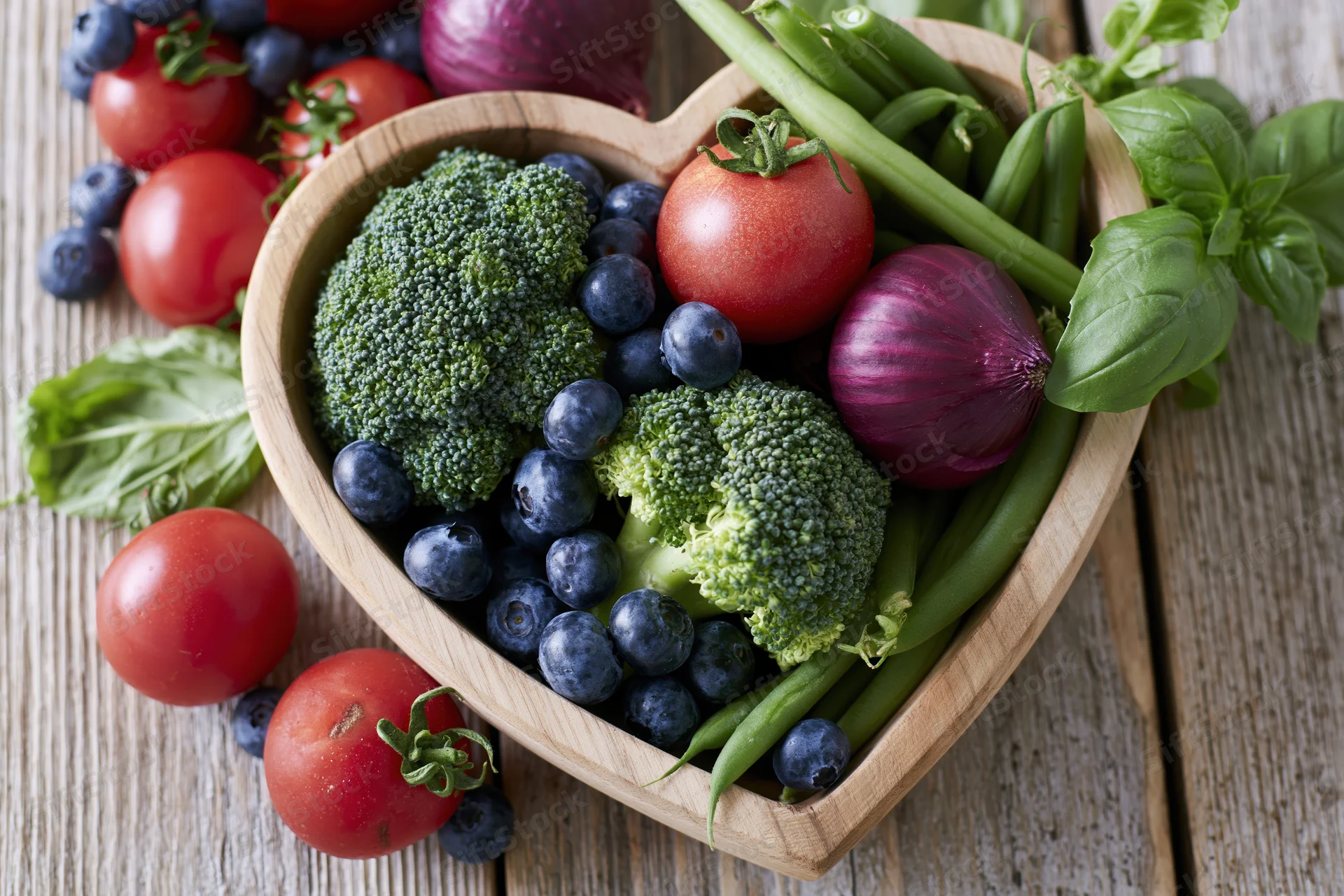Heart-shaped wooden bowl filled with fresh vegetables and berries on a rustic wooden table