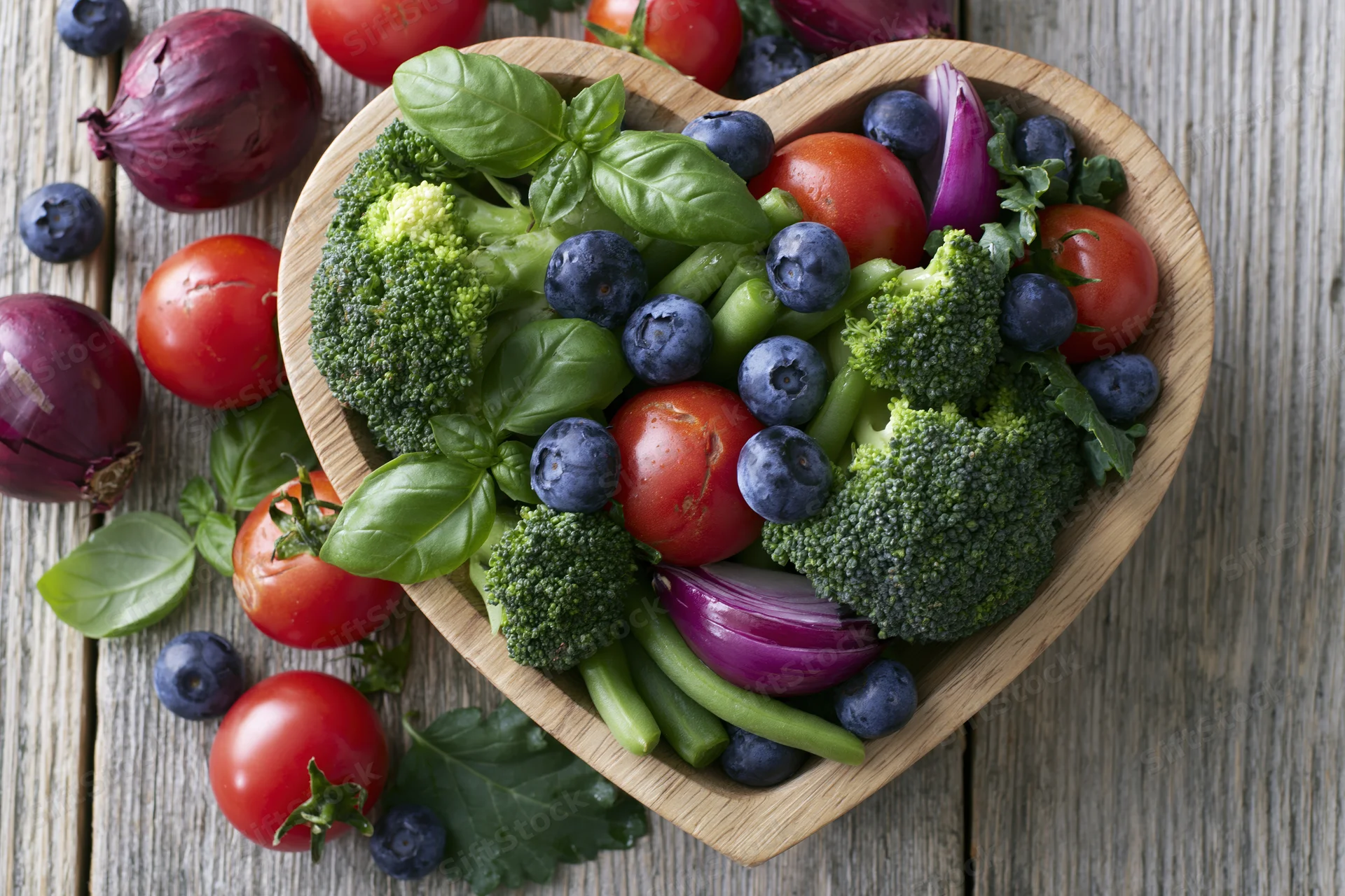 Heart-shaped wooden bowl filled with fresh vegetables and berries on a rustic wooden table