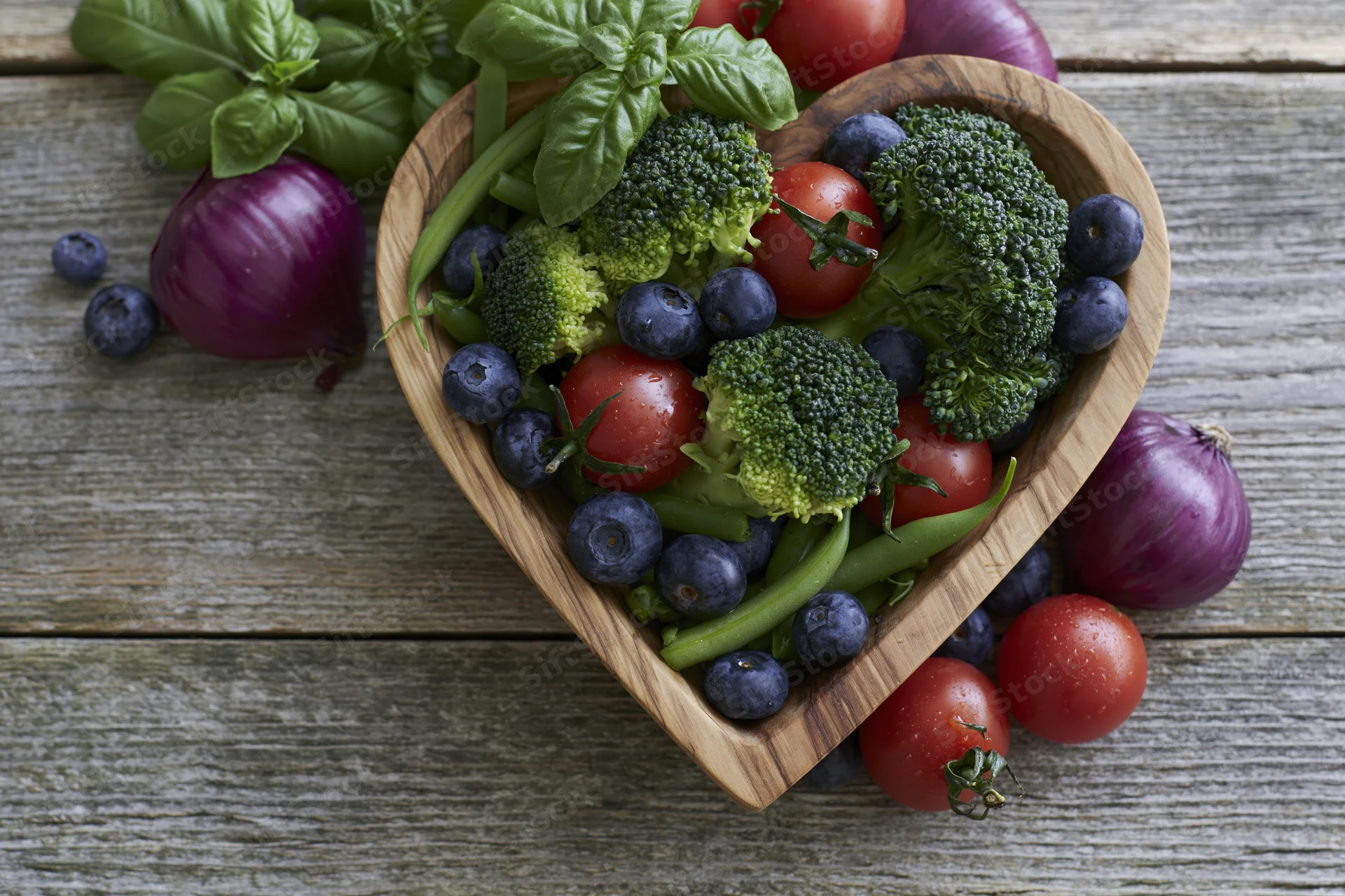 Heart-shaped wooden bowl filled with fresh vegetables and berries on rustic wood surface