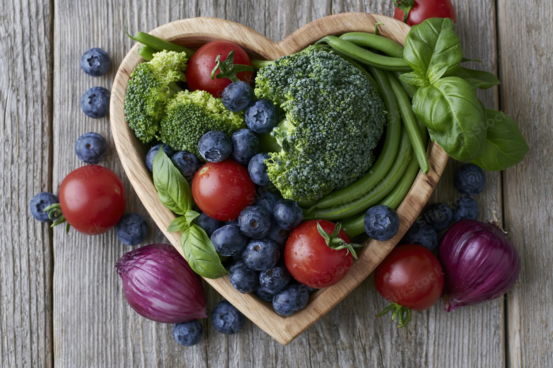 Heart-shaped wooden bowl filled with fresh vegetables and berries on a rustic wooden surface