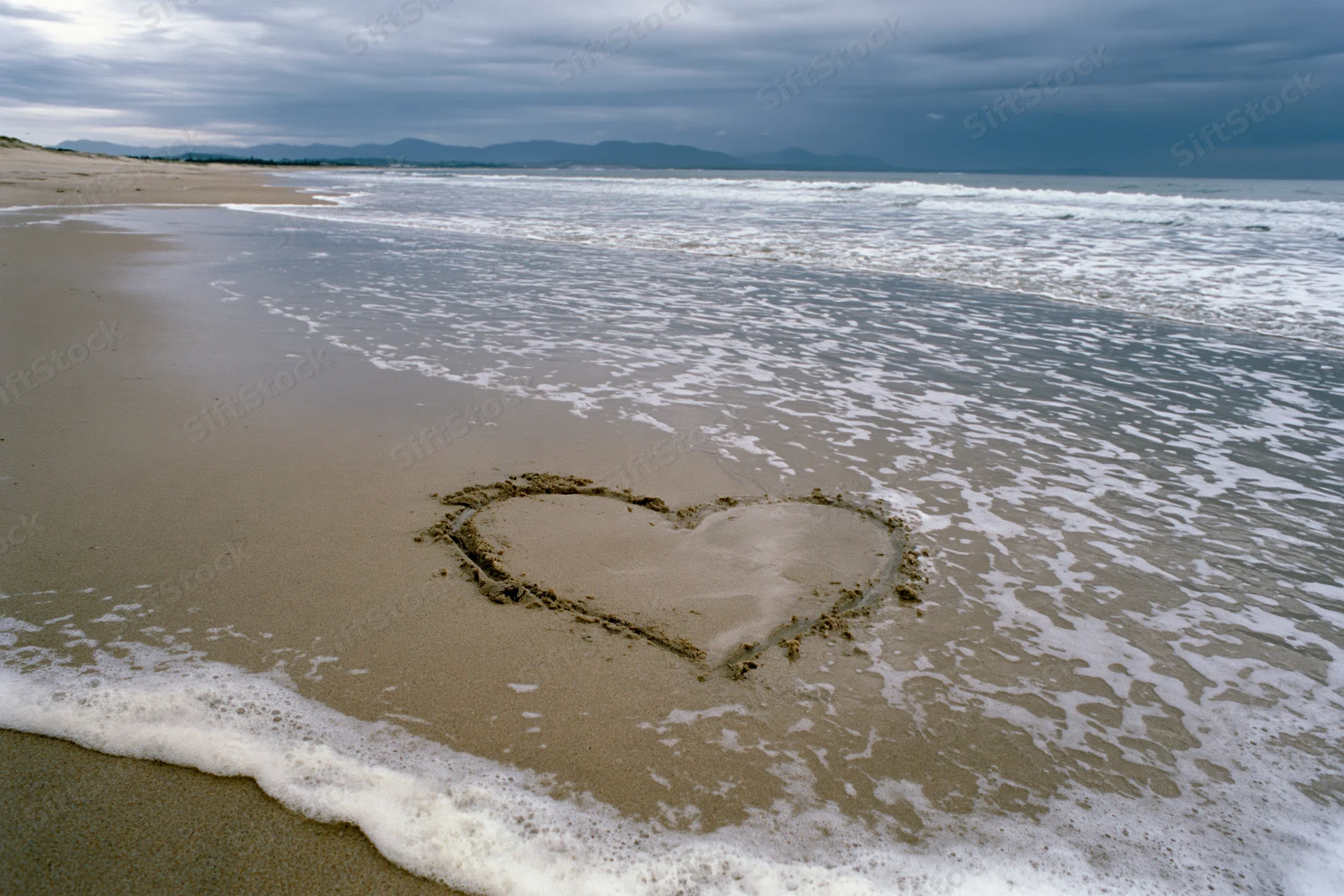 Heart drawn in wet sand on a beach with gentle waves approaching