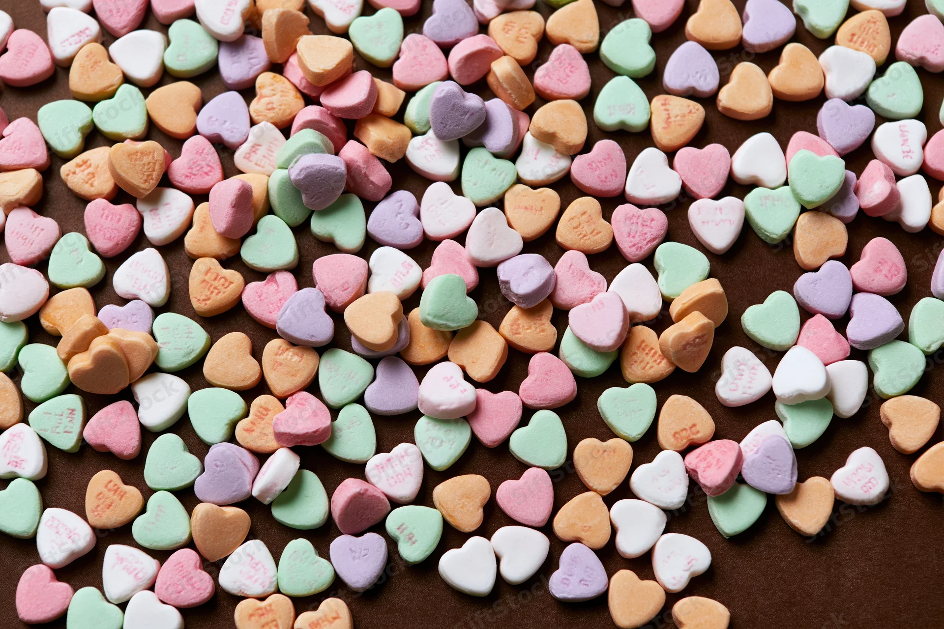 Scattered pastel conversation hearts on brown surface in flat lay view