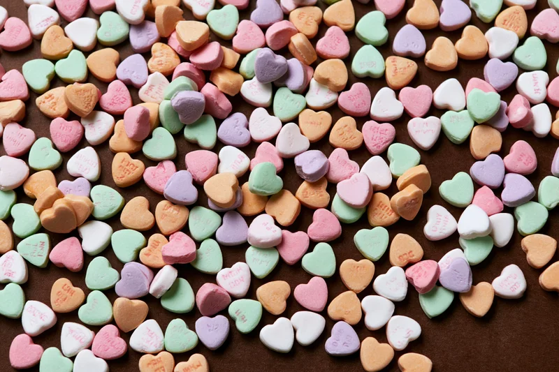 Scattered pastel conversation hearts on brown surface in flat lay view