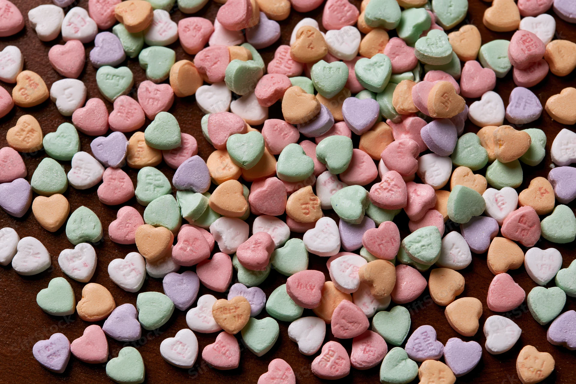 Scattered pastel conversation hearts on a dark surface