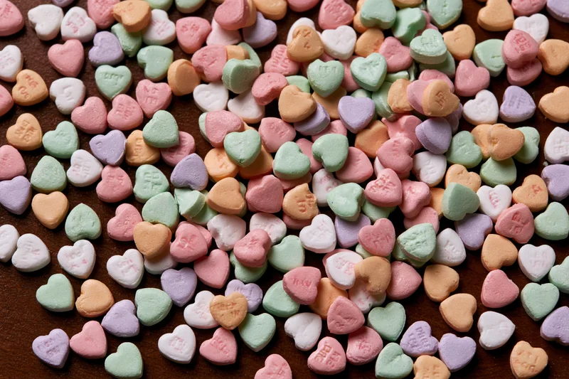Scattered pastel conversation hearts on a dark surface