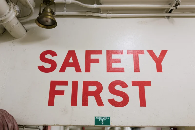Safety first text painted in red on white industrial wall with pipes and lighting above