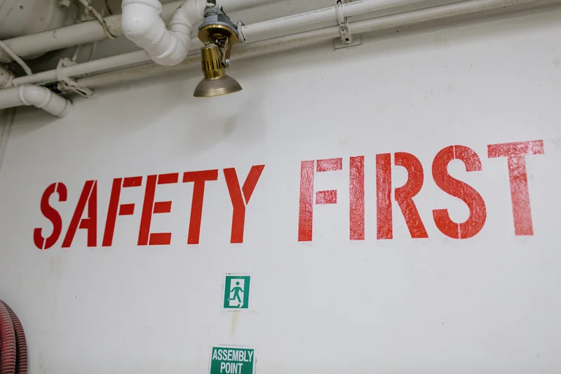 Safety first sign painted in red on white industrial wall with pipes and emergency exit symbols below