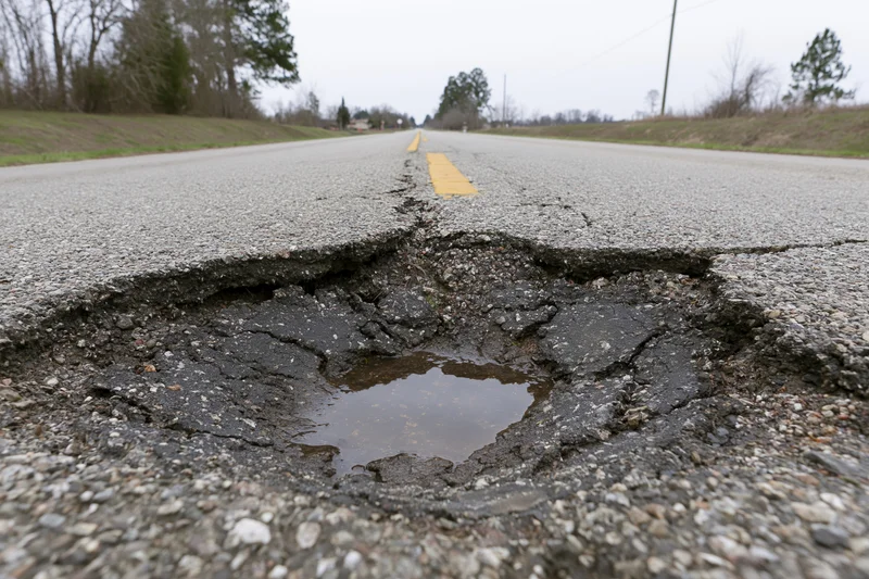 Large pothole with crumbling asphalt edges on a two-lane rural road