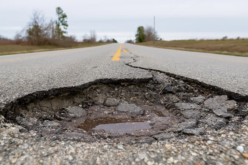 Large pothole with crumbling asphalt edges on a rural two-lane road