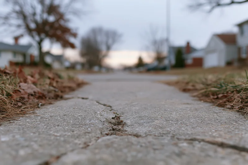 Cracked concrete sidewalk viewed from ground level in suburban neighborhood