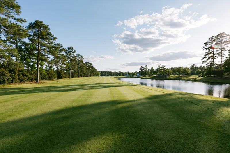 Manicured golf course fairway stretching toward a calm pond under a partly cloudy sky