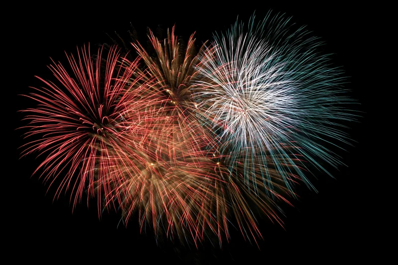 Fireworks bursting in red white and blue forming a heart shape in the night sky