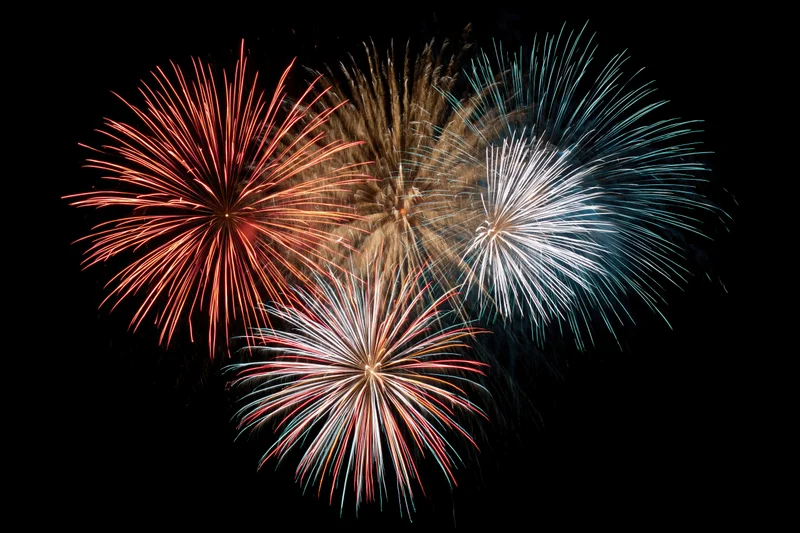 Multiple fireworks bursting in red, white, blue, and gold against dark night sky