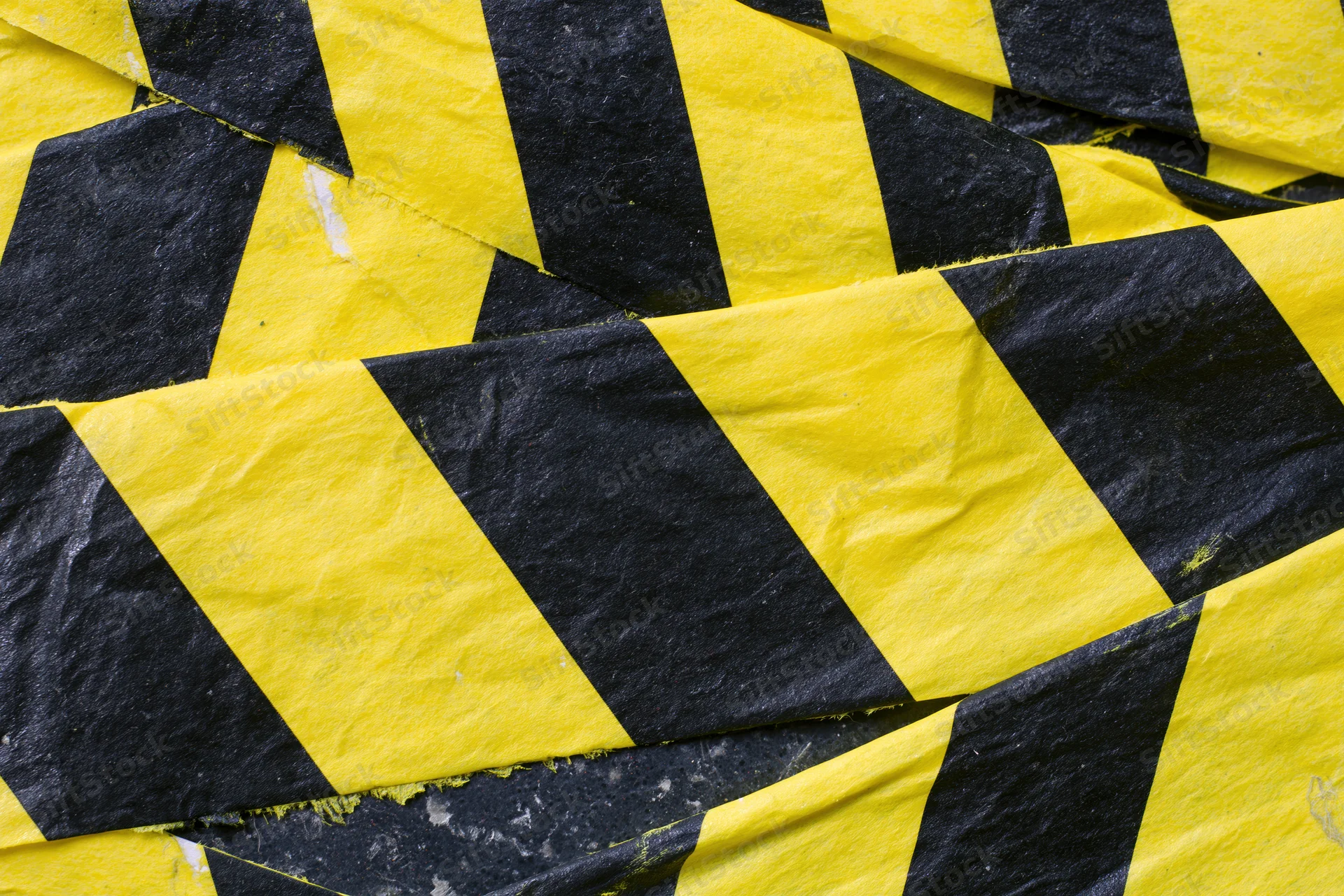 Overlapping strips of yellow and black diagonal hazard tape crumpled on a surface
