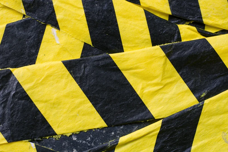 Overlapping strips of yellow and black diagonal hazard tape crumpled on a surface