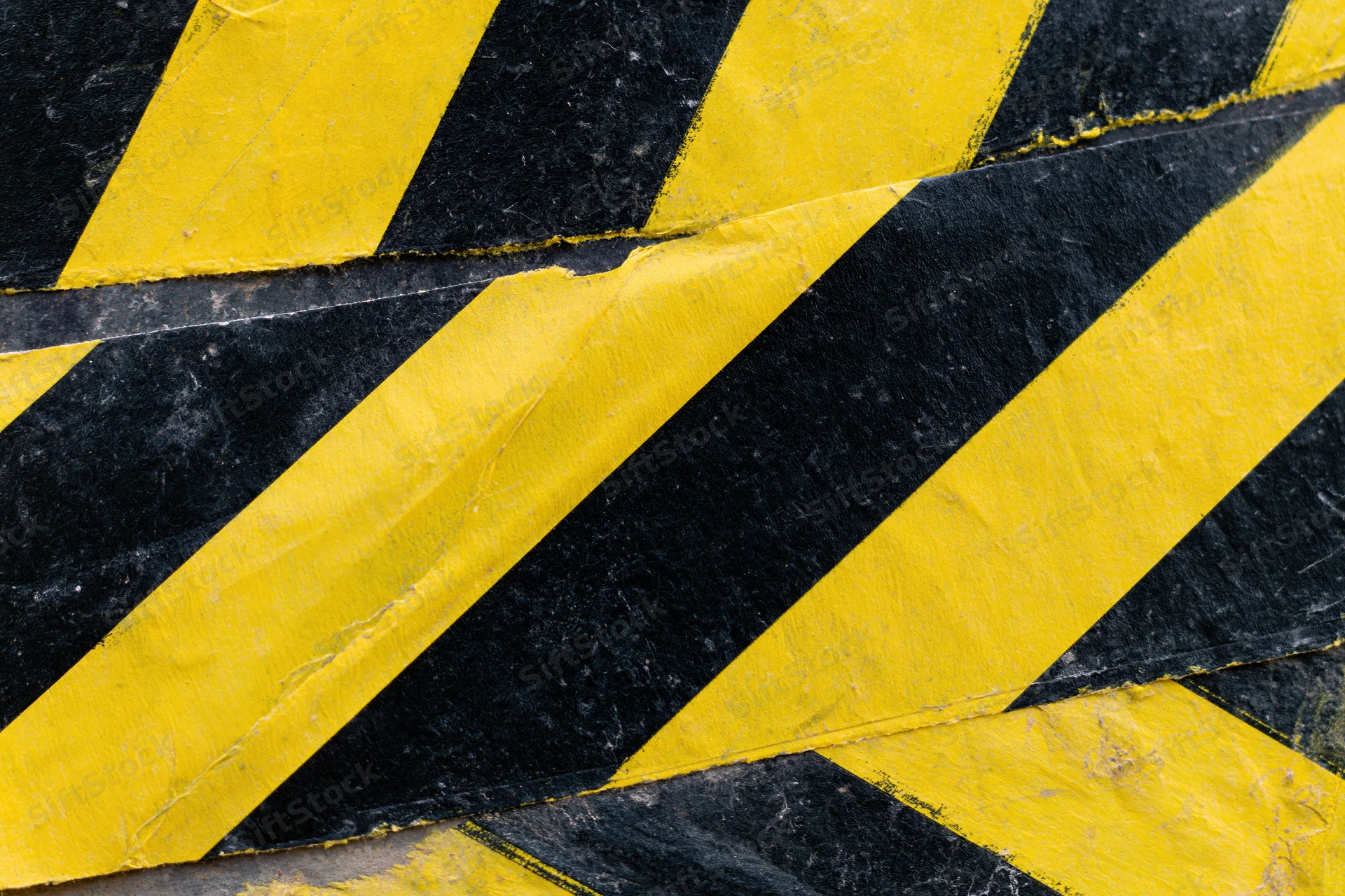 Overlapping strips of yellow and black diagonal hazard tape on a worn surface