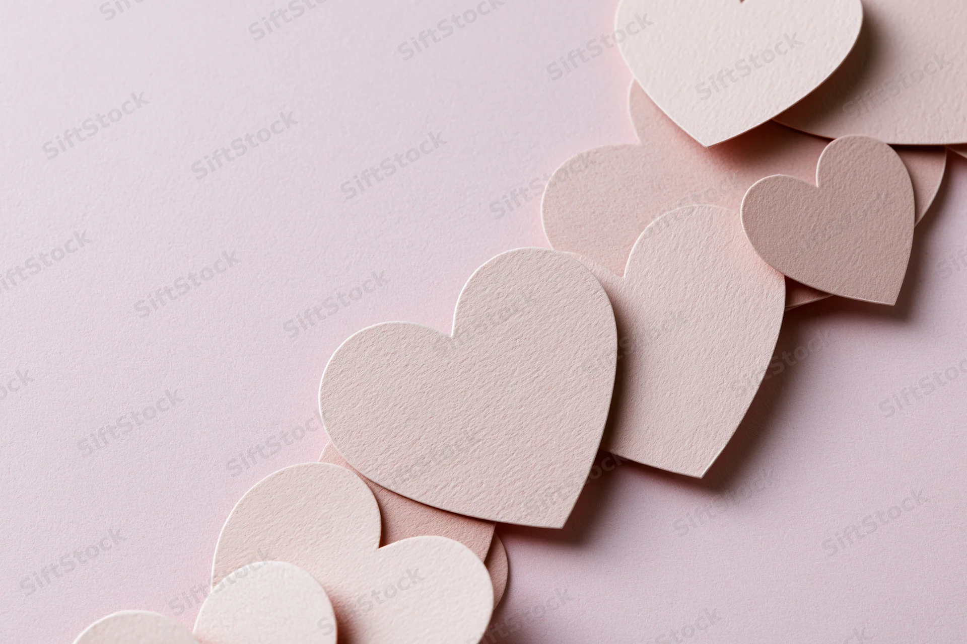 Paper heart cutouts arranged diagonally on a pink surface with copyspace