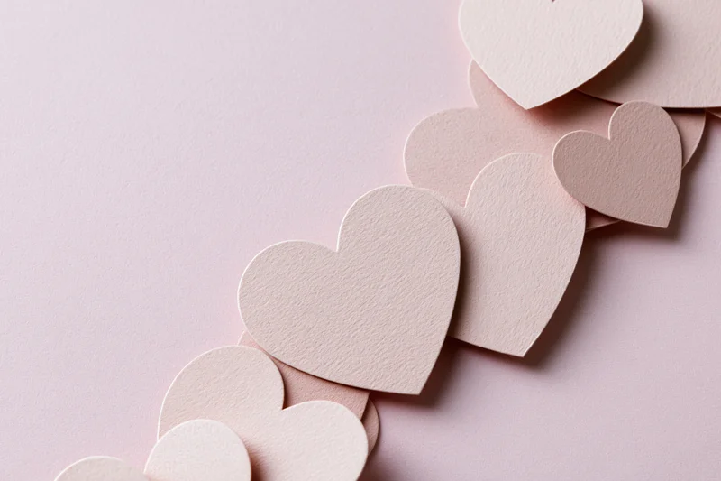Paper heart cutouts arranged diagonally on a pink surface with copyspace