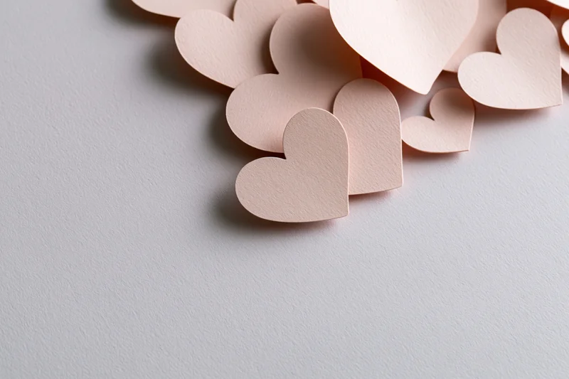 Paper heart cutouts scattered along the top right corner of a white surface
