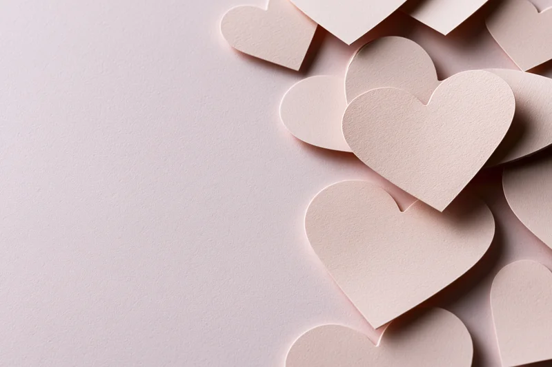Paper heart cutouts arranged along the right side on a light pink surface