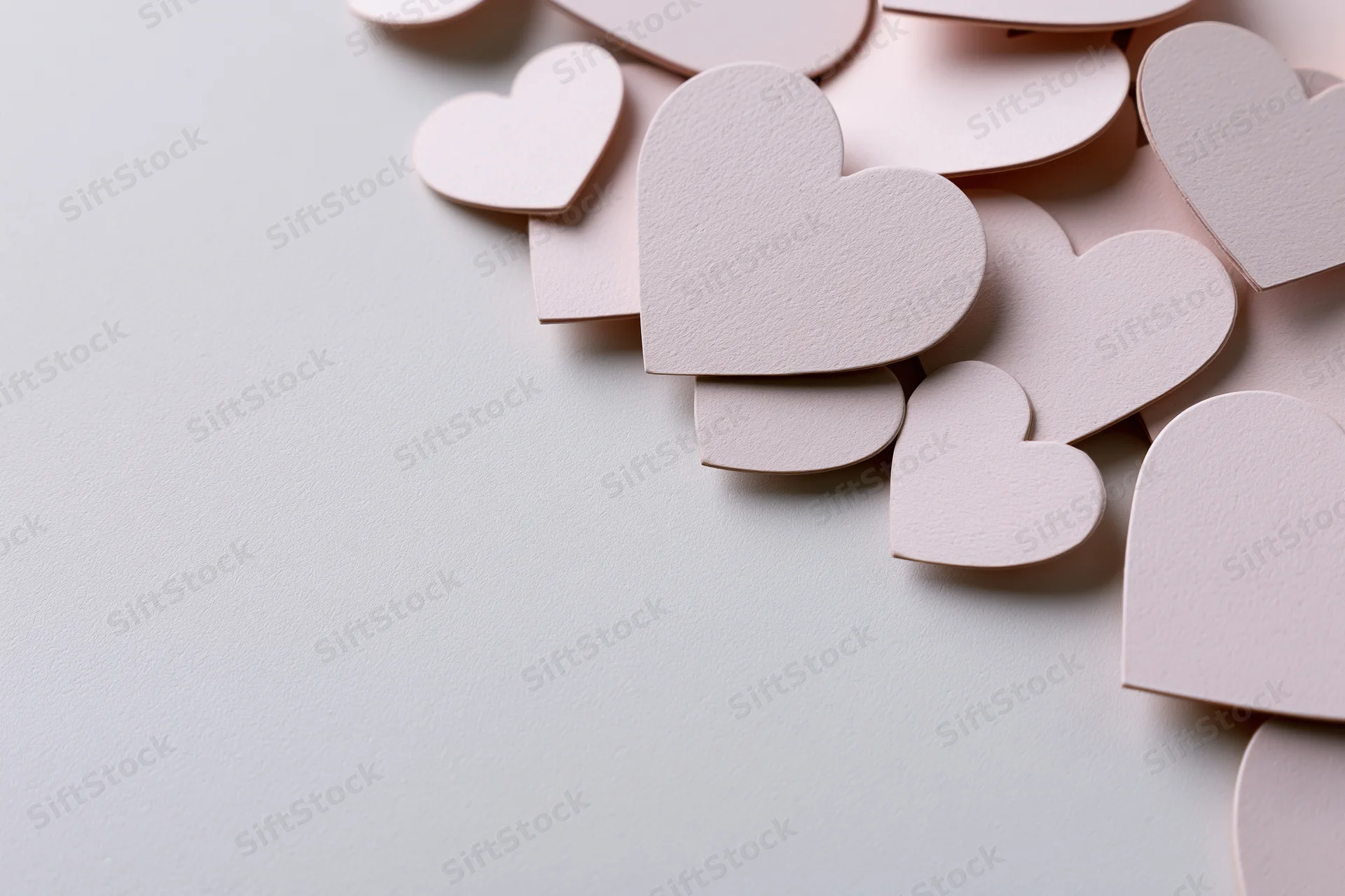 Paper heart cutouts scattered across a white surface with copyspace on the left