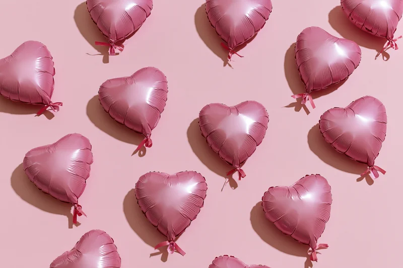 Pink foil heart-shaped balloons arranged on a pastel pink surface in a flat lay composition