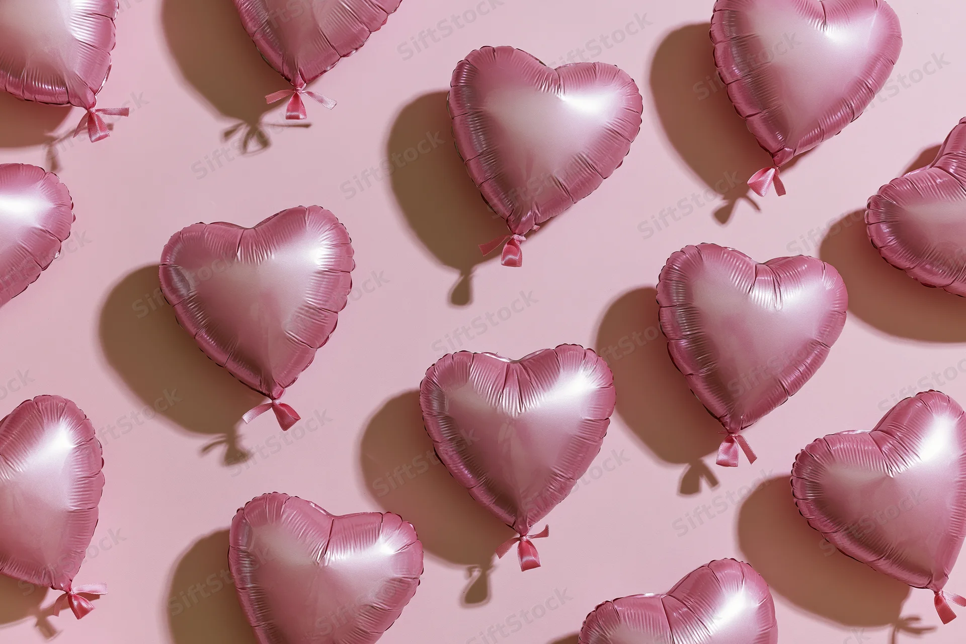 Pink foil heart-shaped balloons arranged in a flat lay pattern on a matching pink surface