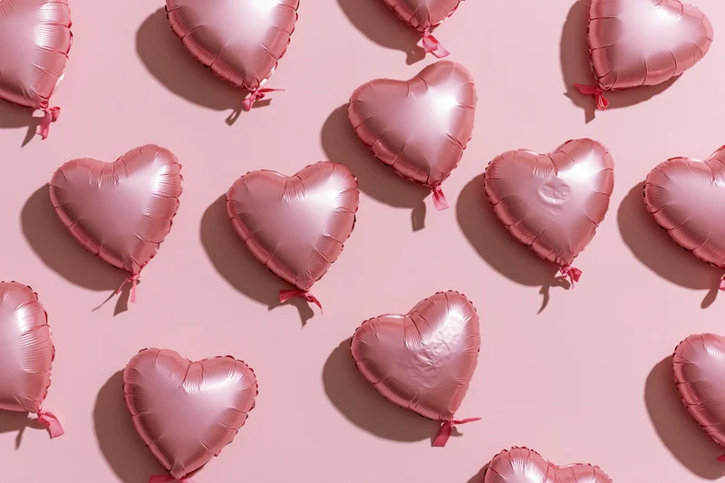 Heart-shaped pink foil balloons arranged flat on a pastel pink surface