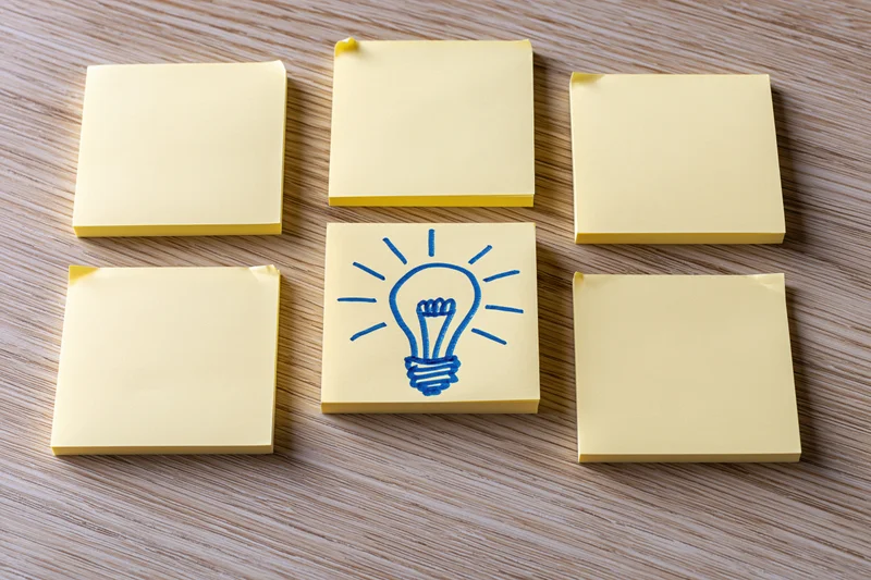 Yellow sticky notes arranged in grid on wooden desk with one featuring blue lightbulb drawing