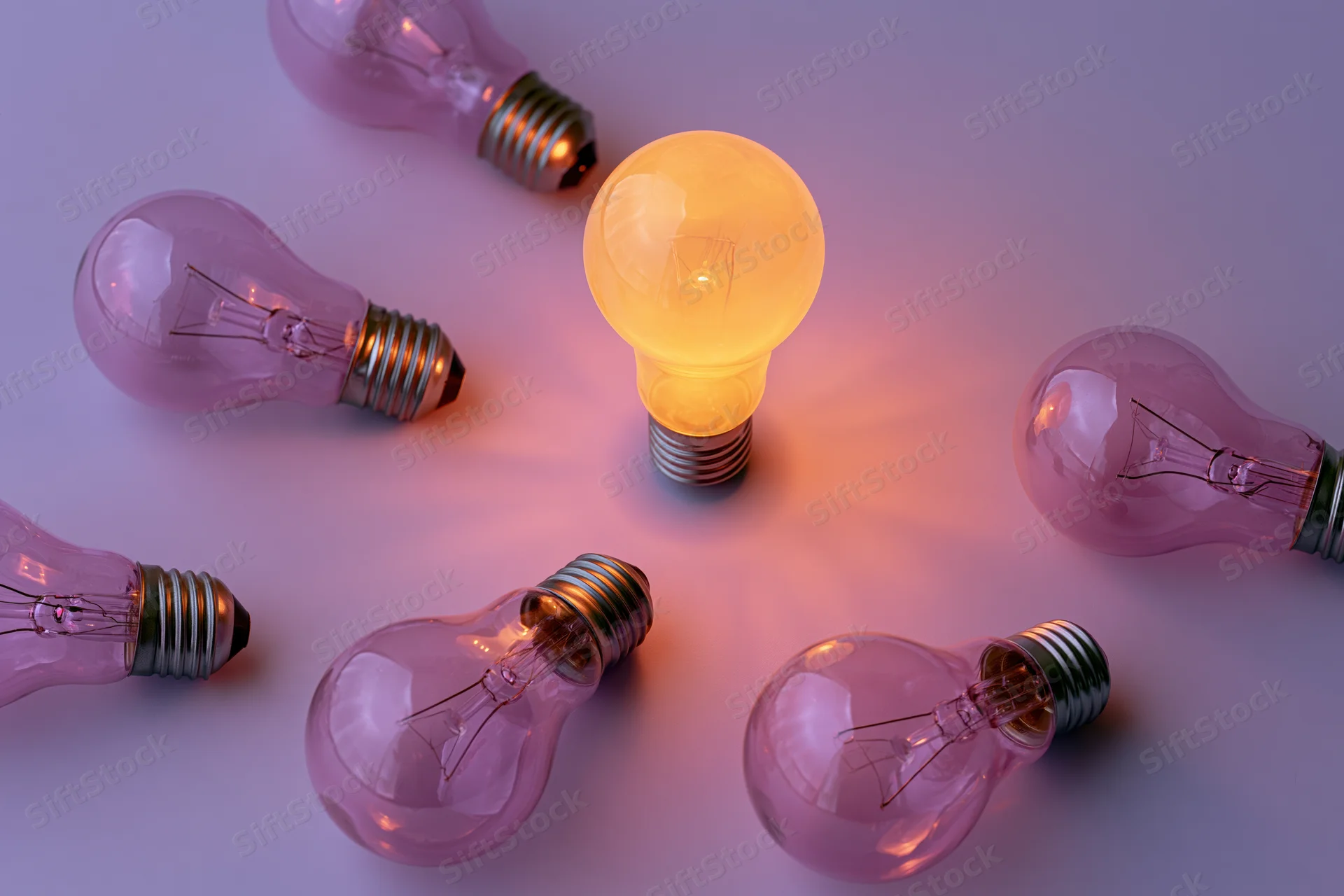 One glowing lightbulb standing upright surrounded by unlit bulbs on a smooth surface