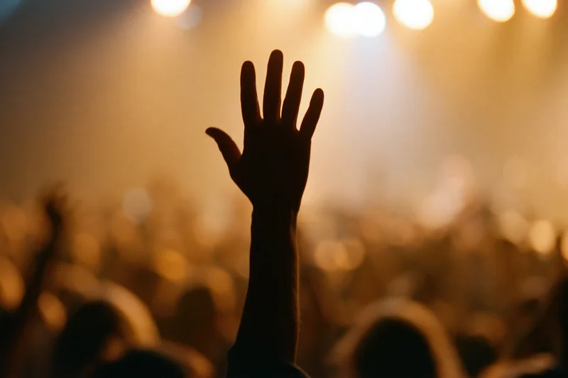 Hand raised in silhouette above a crowd at a concert under stage lights