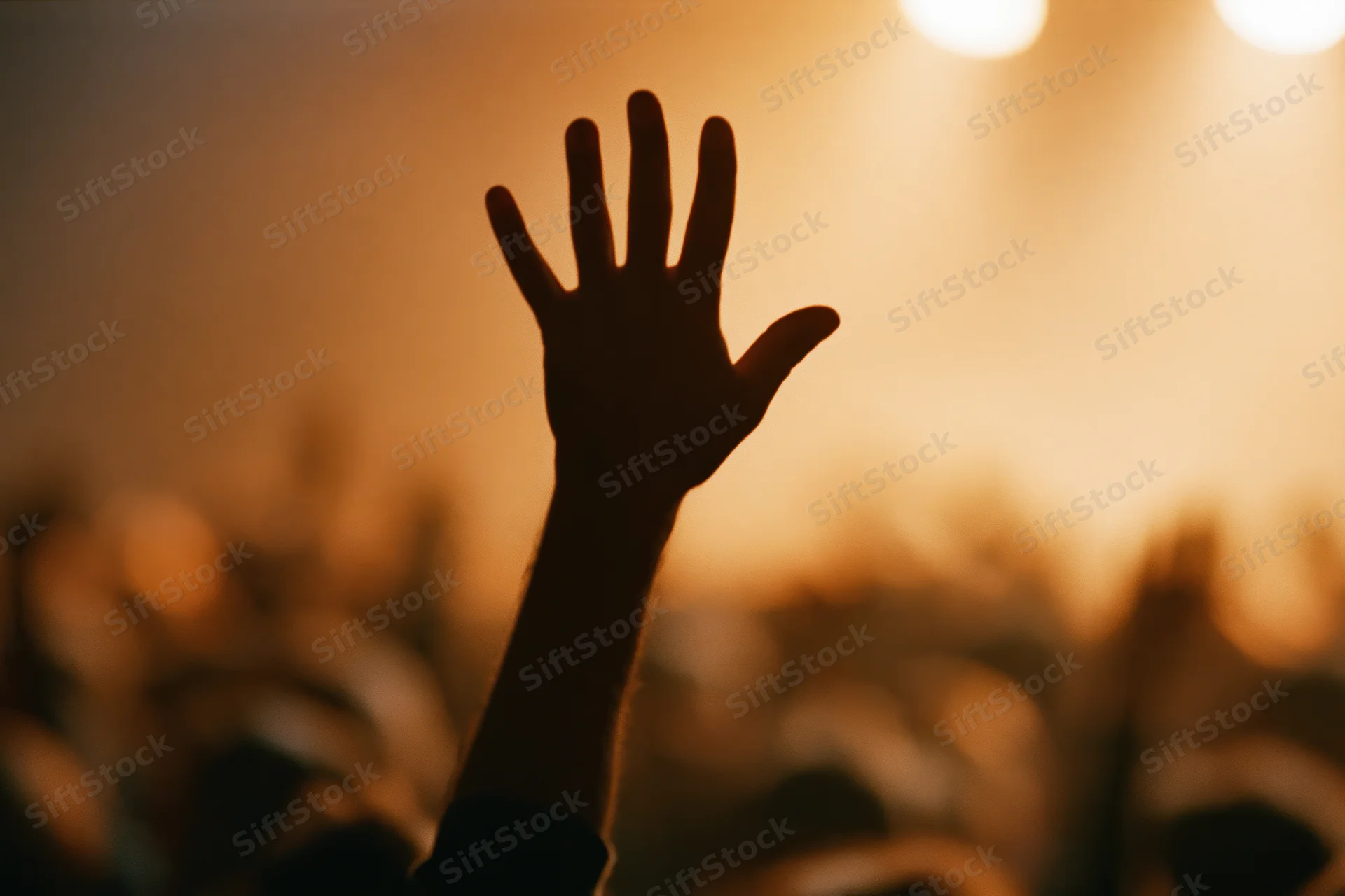 Silhouette of a hand raised high above a blurred crowd at a concert under warm stage lights