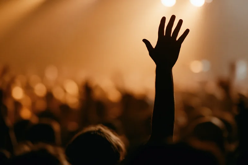 Hand raised high in silhouette above a crowd at a concert under warm stage lights