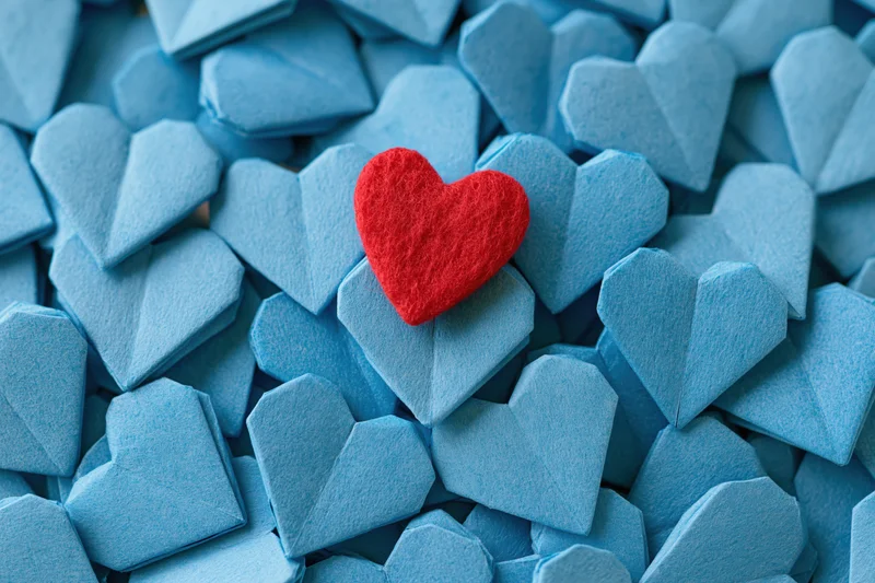 Red felt heart resting on pile of blue origami hearts