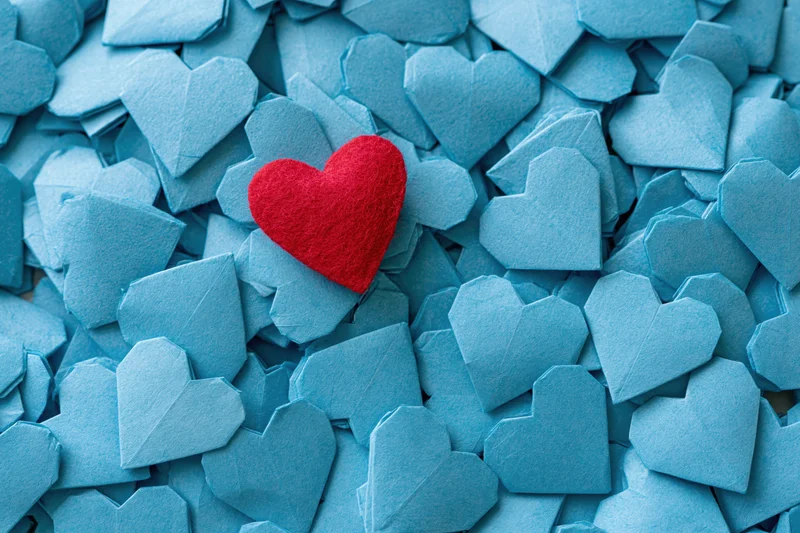 Red felt heart resting on pile of blue paper origami hearts