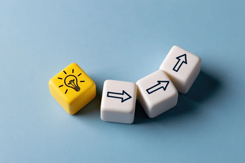 Yellow cube with lightbulb icon and white cubes with arrows arranged in a line on blue surface