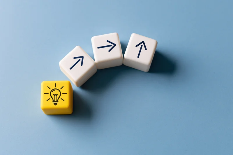 Yellow cube with lightbulb icon and three white cubes with arrows arranged in arc on blue surface