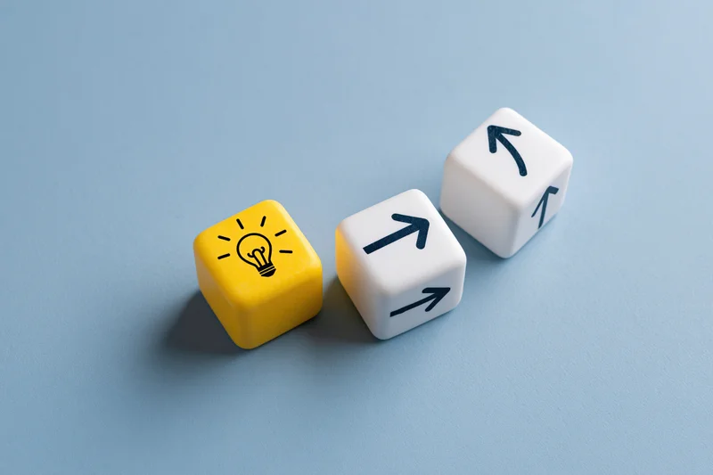 Three cubes with lightbulb and arrow symbols arranged on a blue surface