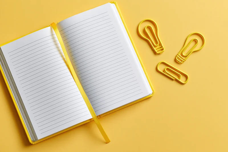 Open blank lined notebook with yellow lightbulb-shaped paperclips on yellow surface