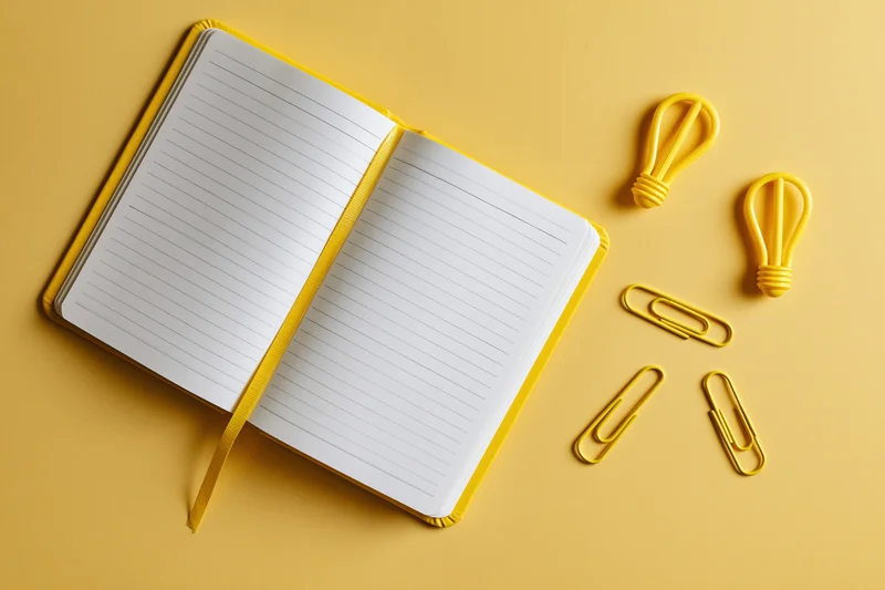 Open lined notebook with yellow paperclips and lightbulb shapes on a yellow surface