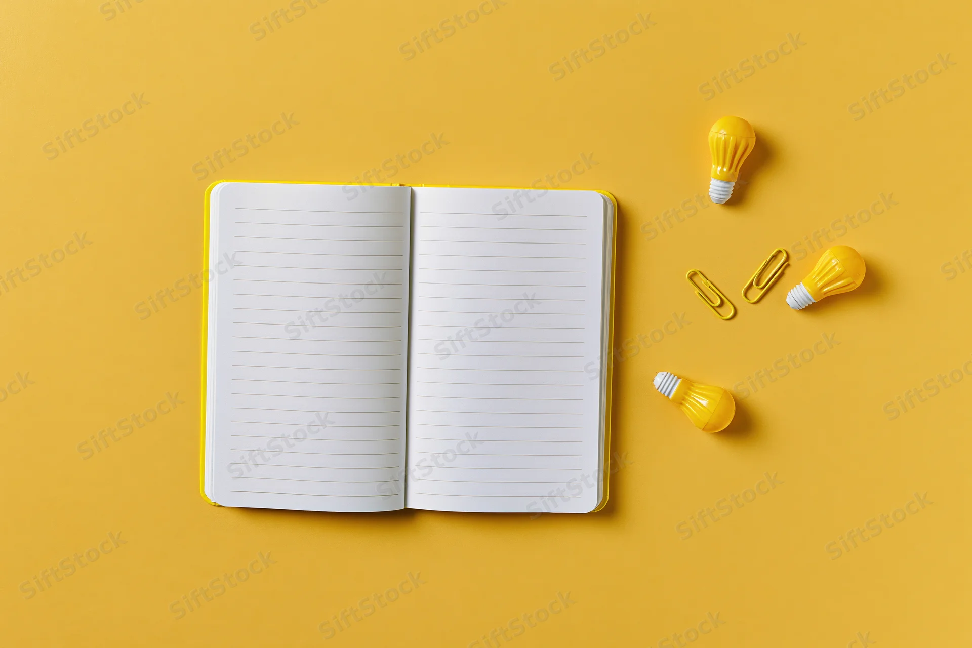 Open blank lined notebook with yellow lightbulbs and paperclips on yellow surface