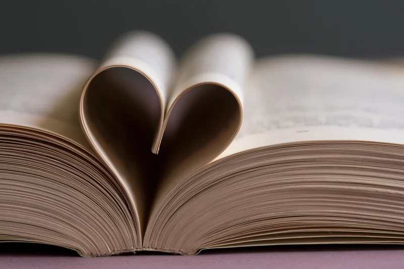 Open book with pages folded into a heart shape on a flat surface