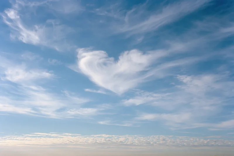Heart-shaped cloud formation in open daytime sky with scattered wispy cirrus clouds