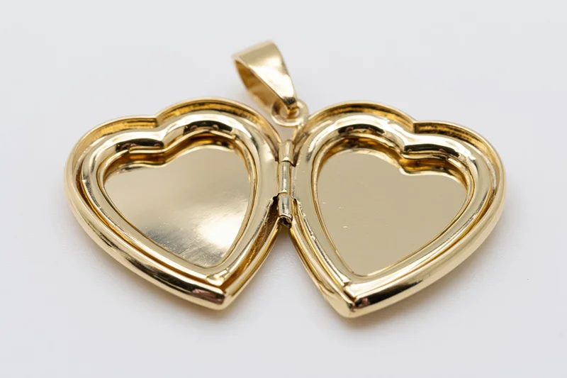 Open gold heart-shaped locket pendant lying flat with both halves visible on white background
