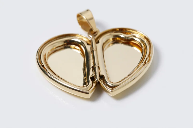 Open gold heart-shaped locket pendant lying flat on white surface