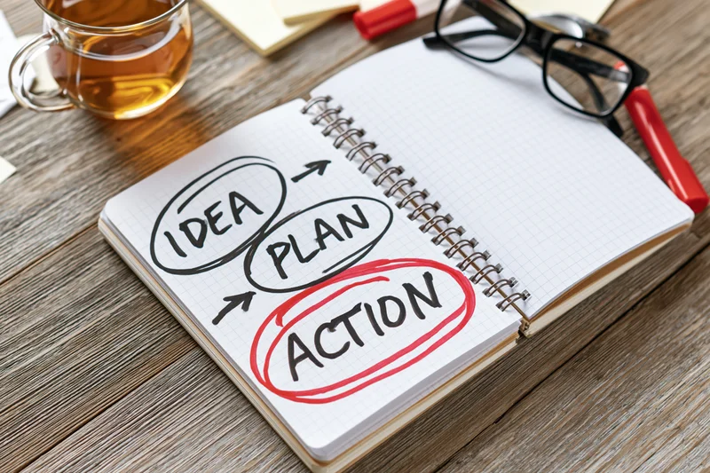 Spiral notebook with hand-drawn idea-plan-action diagram on wooden desk