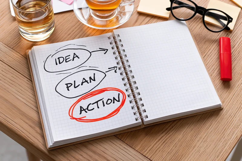 Open spiral notebook with hand-drawn idea-plan-action diagram on wooden desk