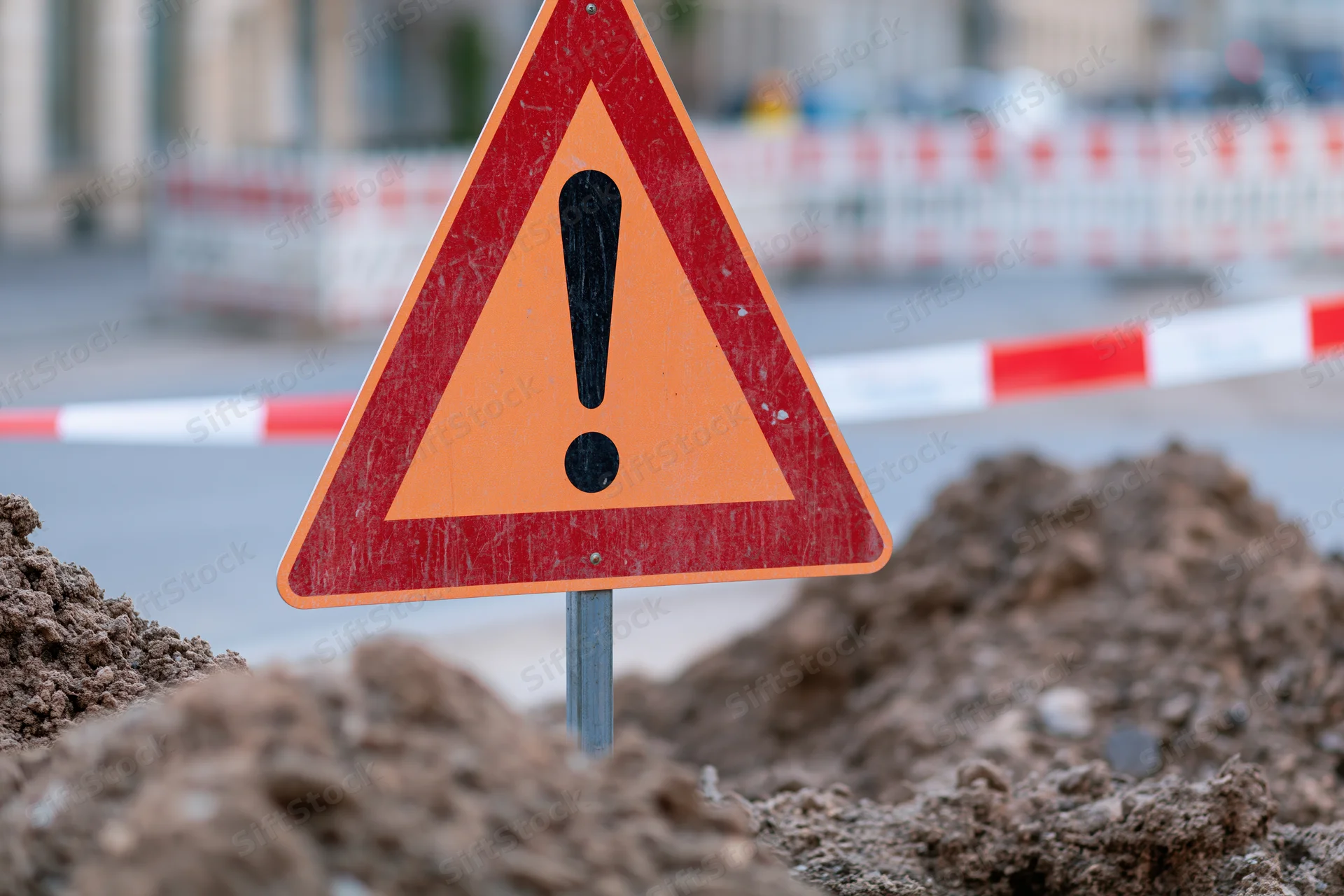 Triangular warning sign with exclamation mark in dirt at construction site
